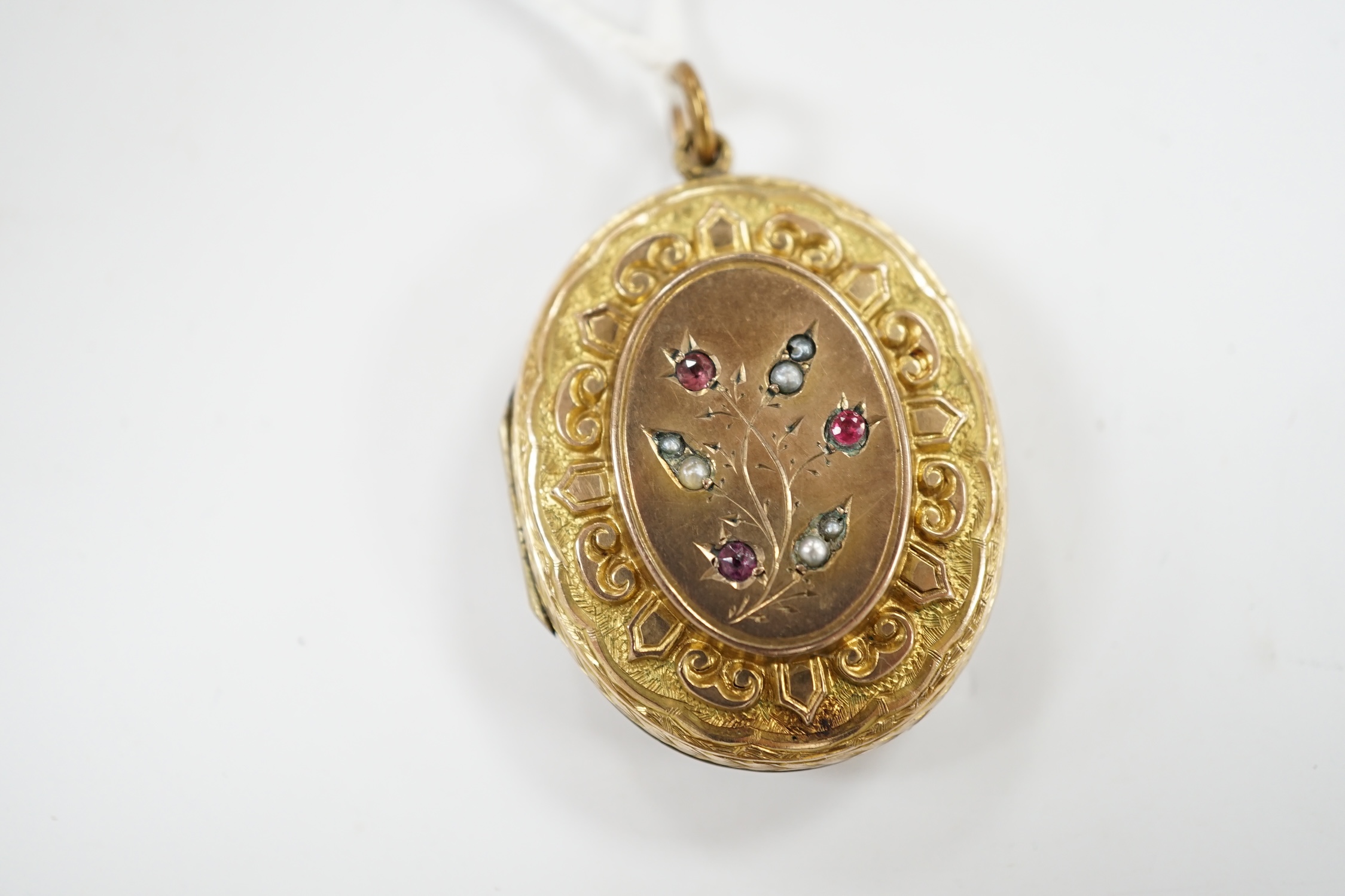 A Victorian engraved yellow metal overlaid, garnet and seed pearl set oval locket, 37mm. Condition - fair